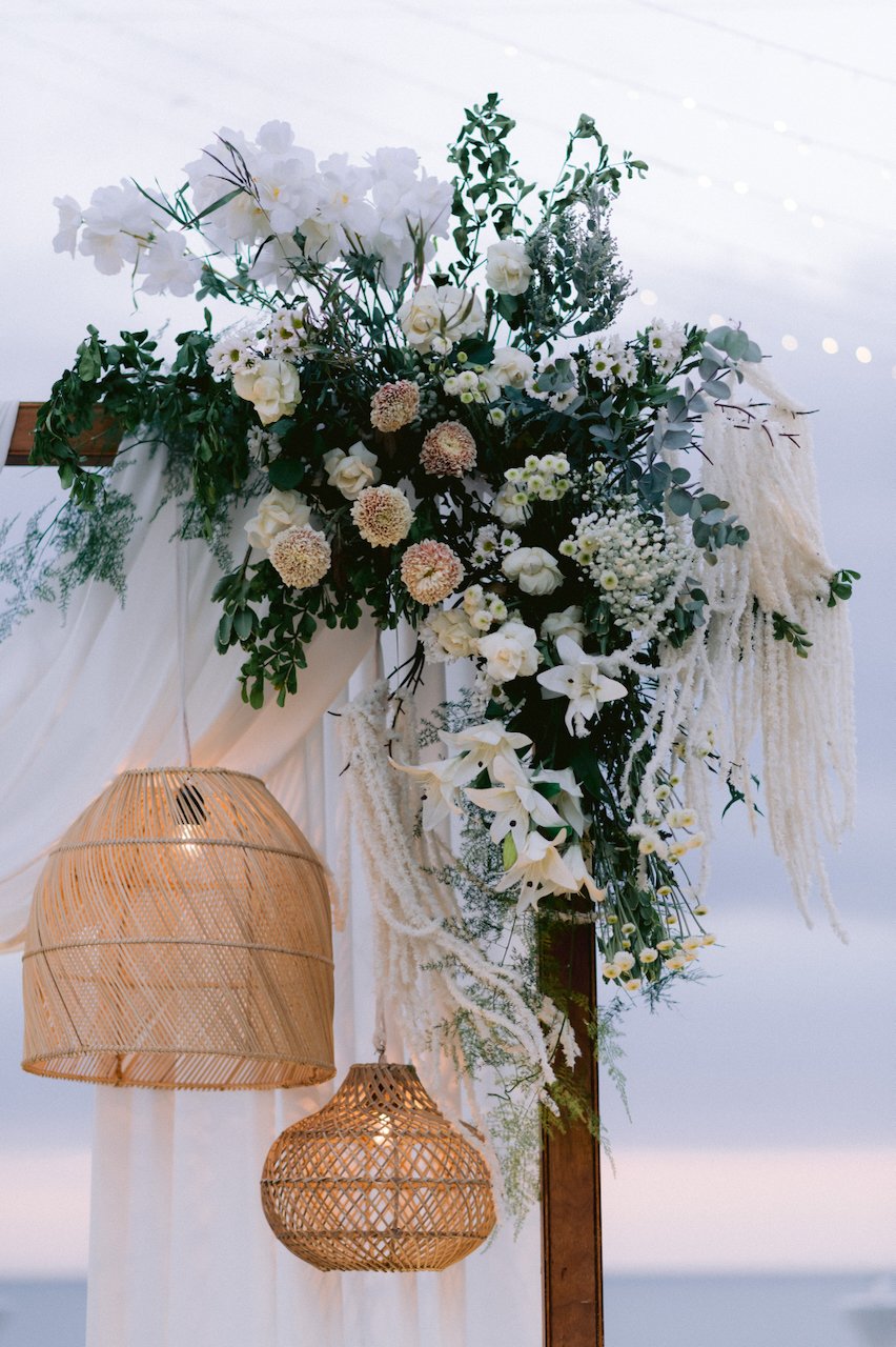 White orchid floral arrangement and rattan lamps hanging at an outdoor wedding