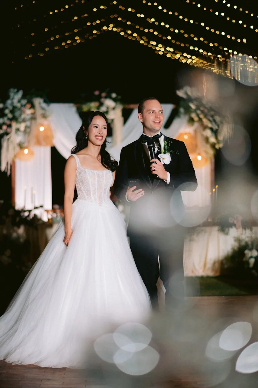 Felicia and Forrest entering their outdoor wedding reception under a fairy light canopy