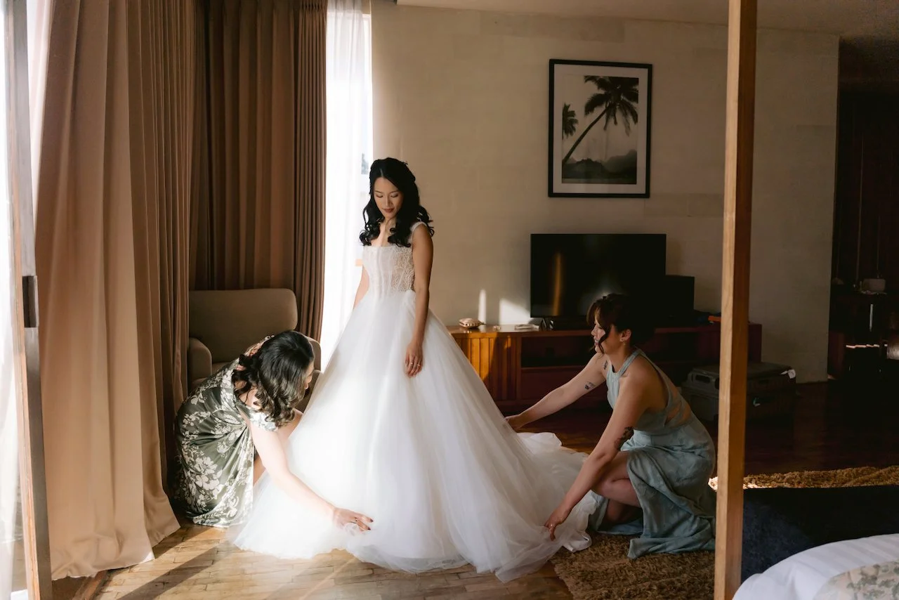 Bridesmaids helping the bride put on her wedding gown in a hotel suite