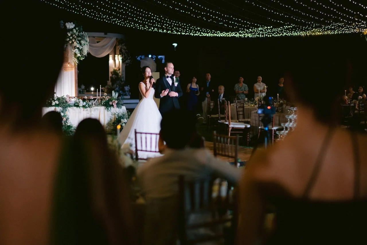 Wedding guests seated for an outdoor dinner reception under a canopy of fairy lights