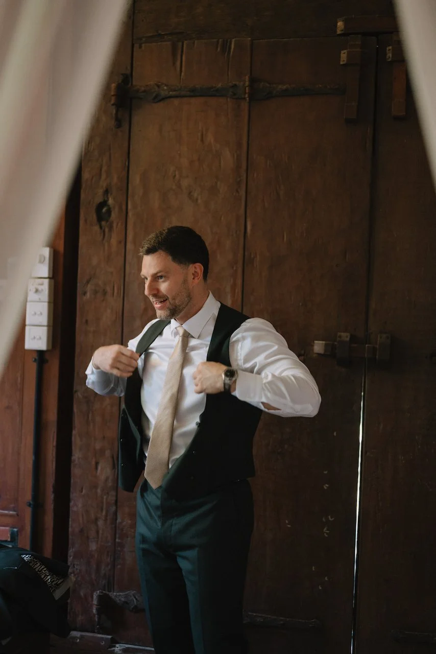 Groom David adjusting his suspenders while getting ready in a wooden villa suite