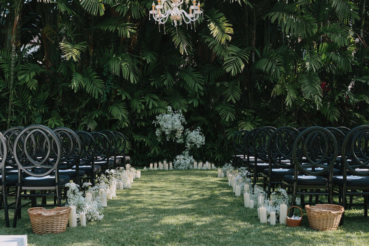 Outdoor wedding ceremony aisle lined with white flowers and black chairs