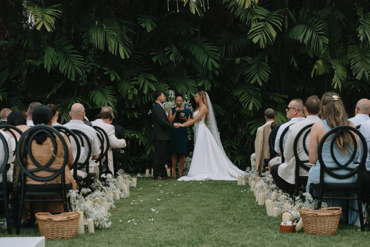 Catherine and David exchanging vows in front of a tropical green foliage wall
