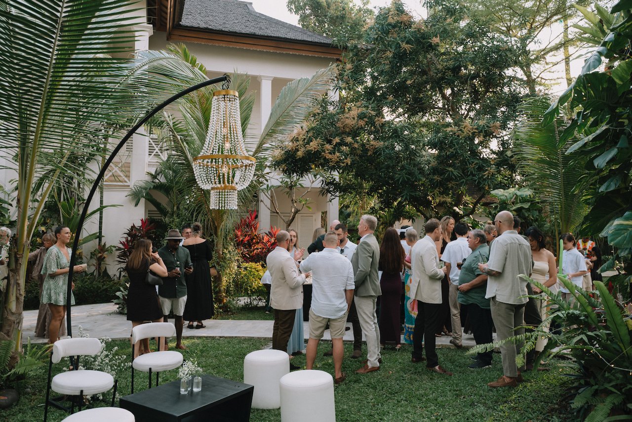Guests mingling during an outdoor cocktail hour under large tropical trees