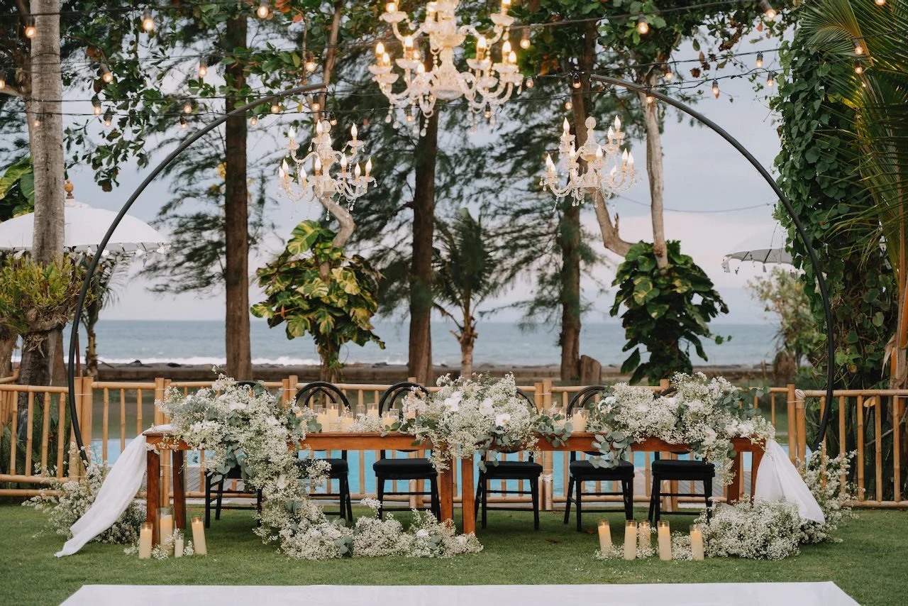 Long wooden reception tables set up under an arched structure with crystal chandeliers