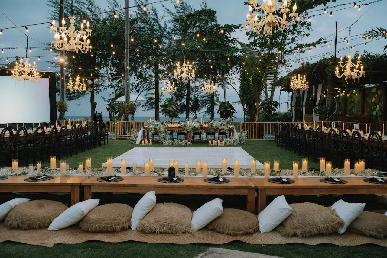 Outdoor wedding reception setup with wooden tables and floor cushions on the grass