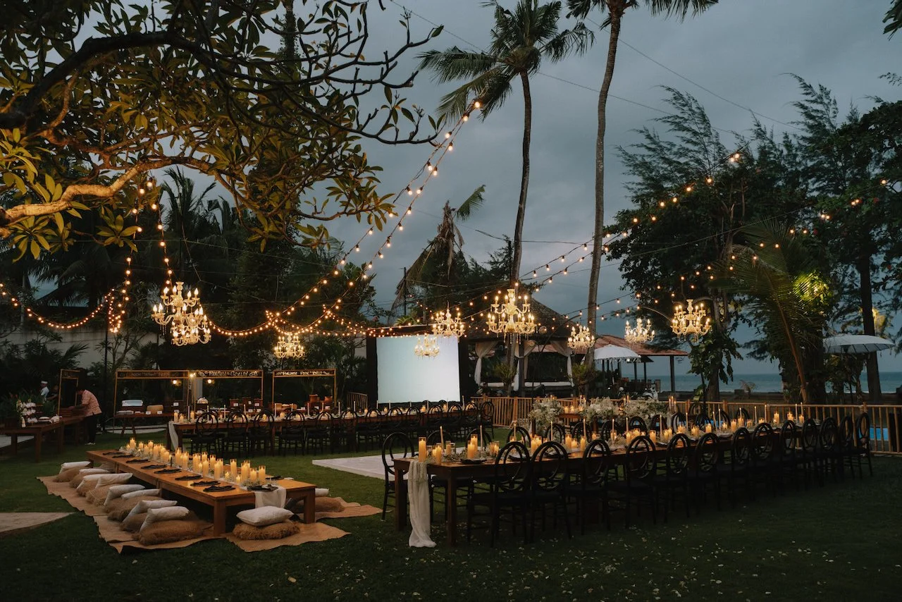 Outdoor wedding reception setup with wooden tables and floor cushions on the grass