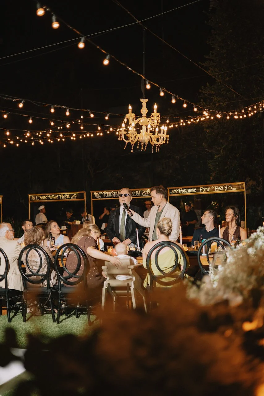 Wedding guests seated at an outdoor dinner reception under warm string lights