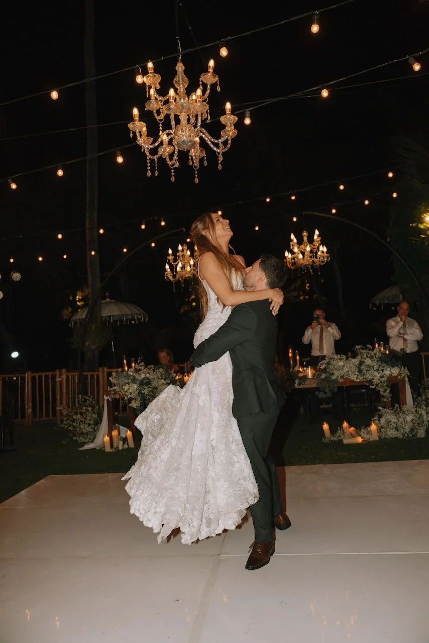 Groom lifting his bride during their first dance on a white outdoor dance floor