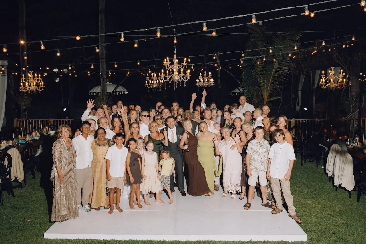 Large group photo of wedding guests gathered on a white dance floor at night