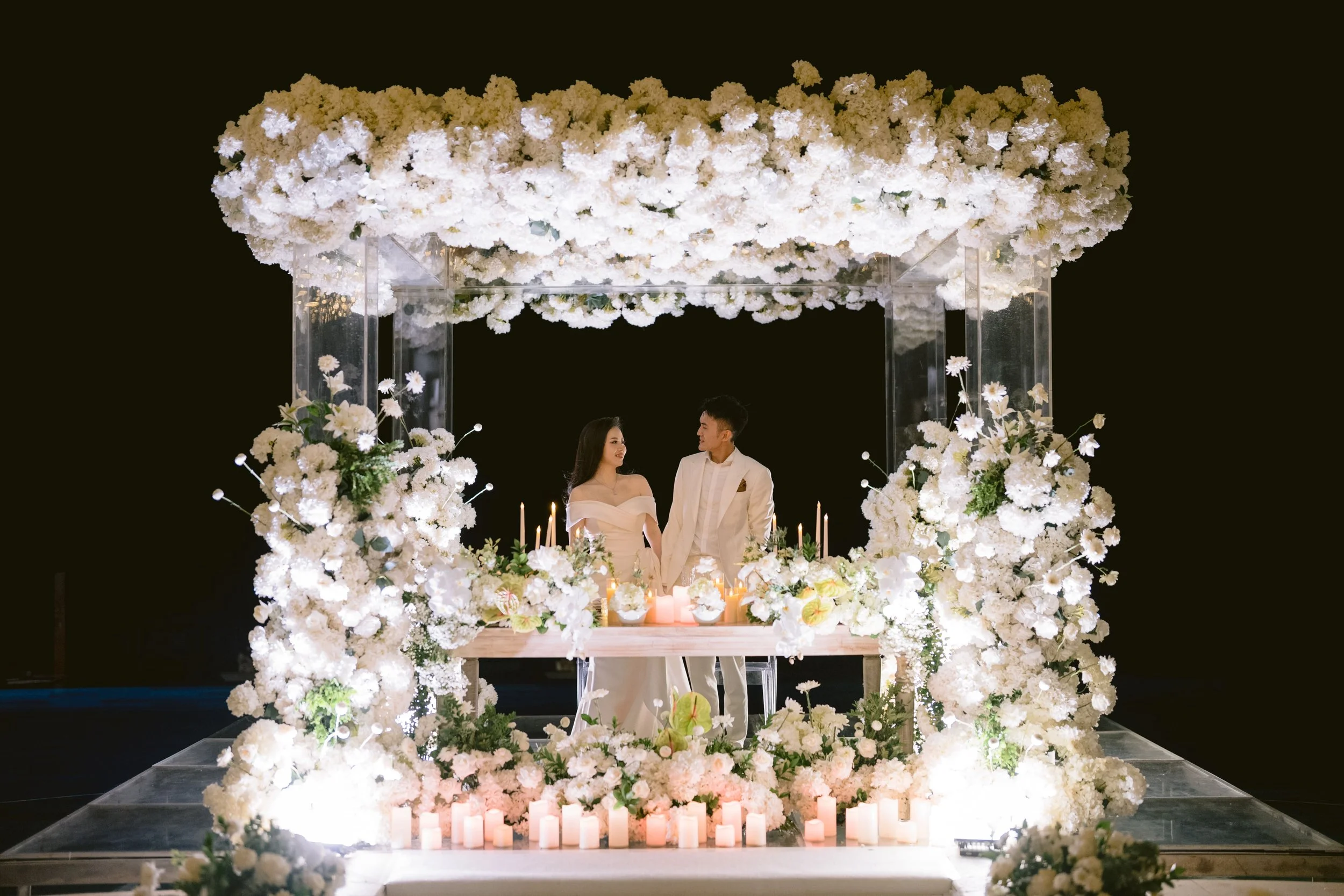 luxury Bali wedding reception couple standing under floral canopy with candles and white floral styling at night
