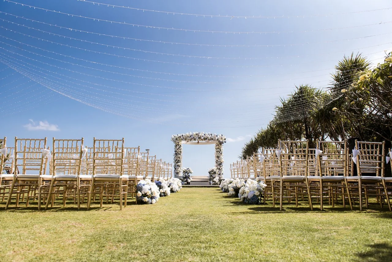 Outdoor wedding aisle lined with white floral arrangements
