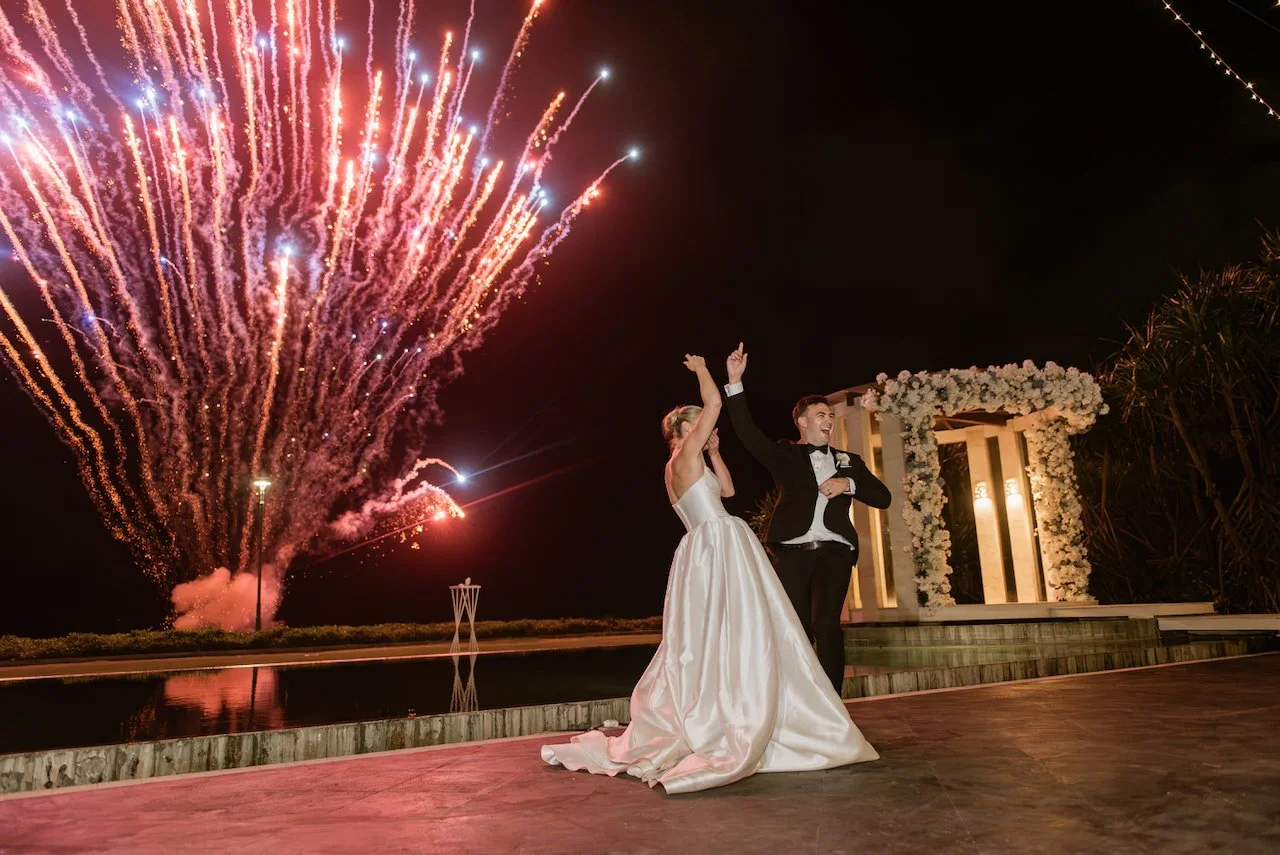 Bride and groom standing together as fireworks light up the sky