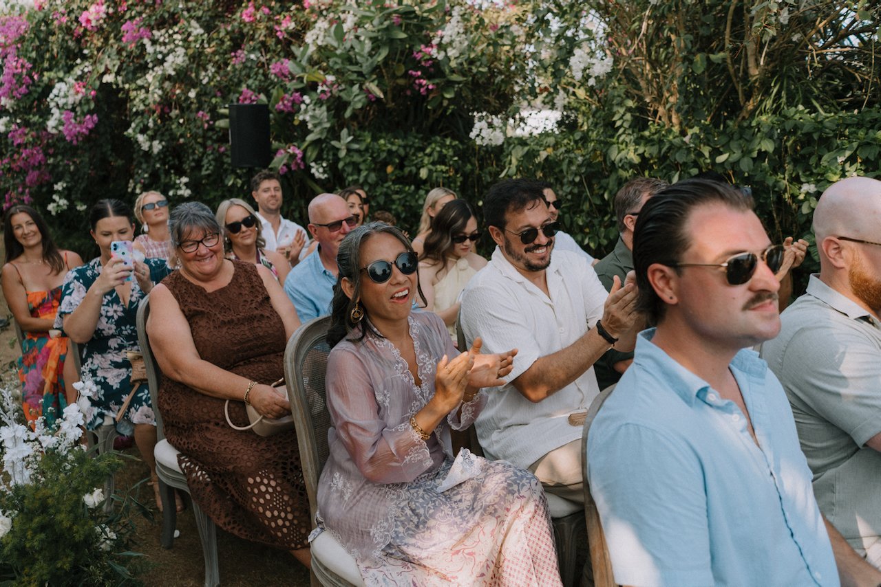 Guests in sunglasses clapping and smiling during the wedding ceremony