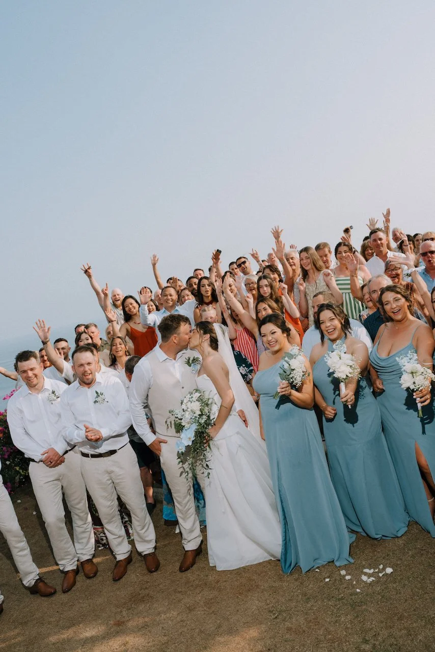 Kelly and Matt kissing in front of their wedding party and guests with their arms in the air, on the Uluwatu clifftop