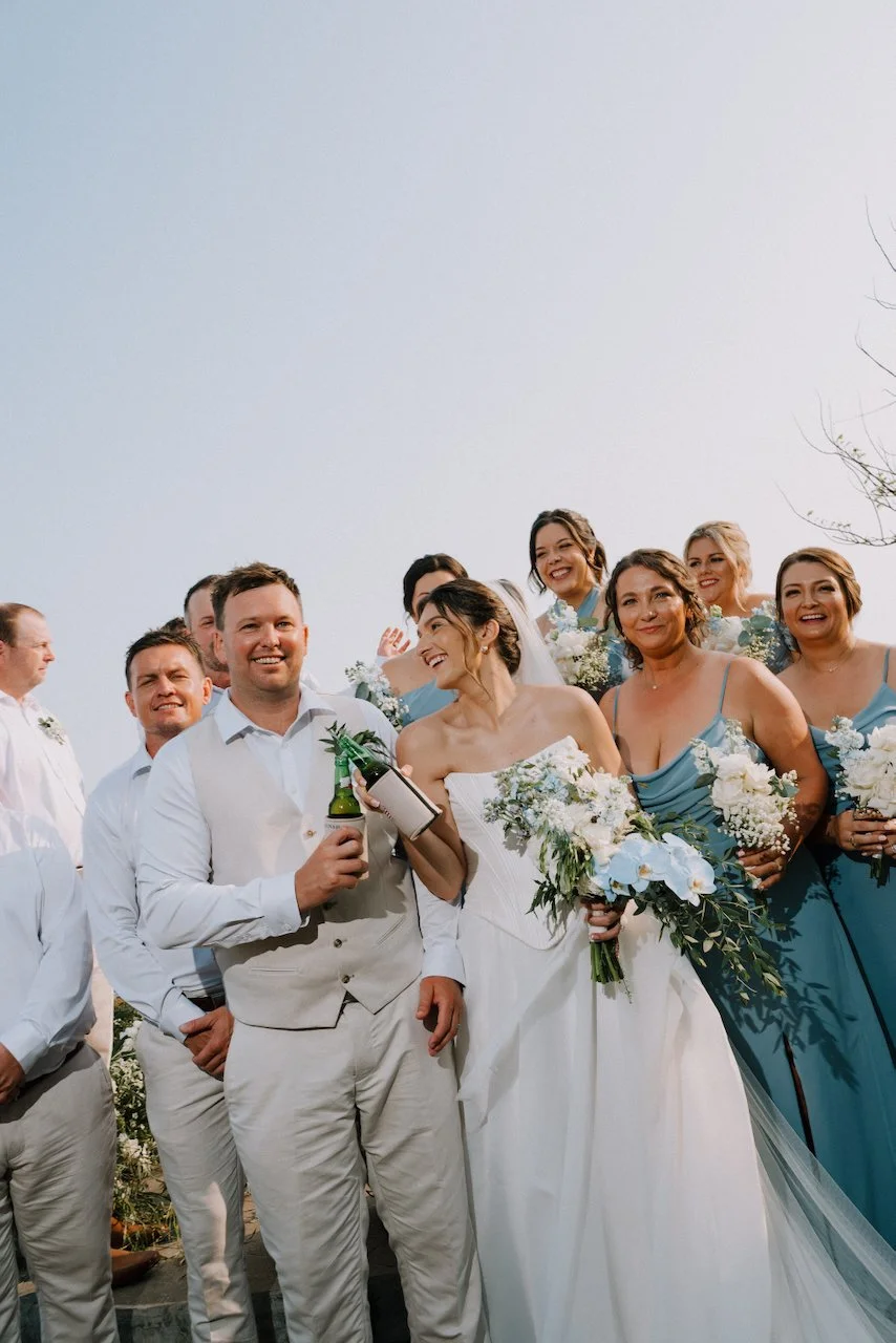 Matt holding a beer and smiling beside Kelly, surrounded by bridesmaids in blue and groomsmen