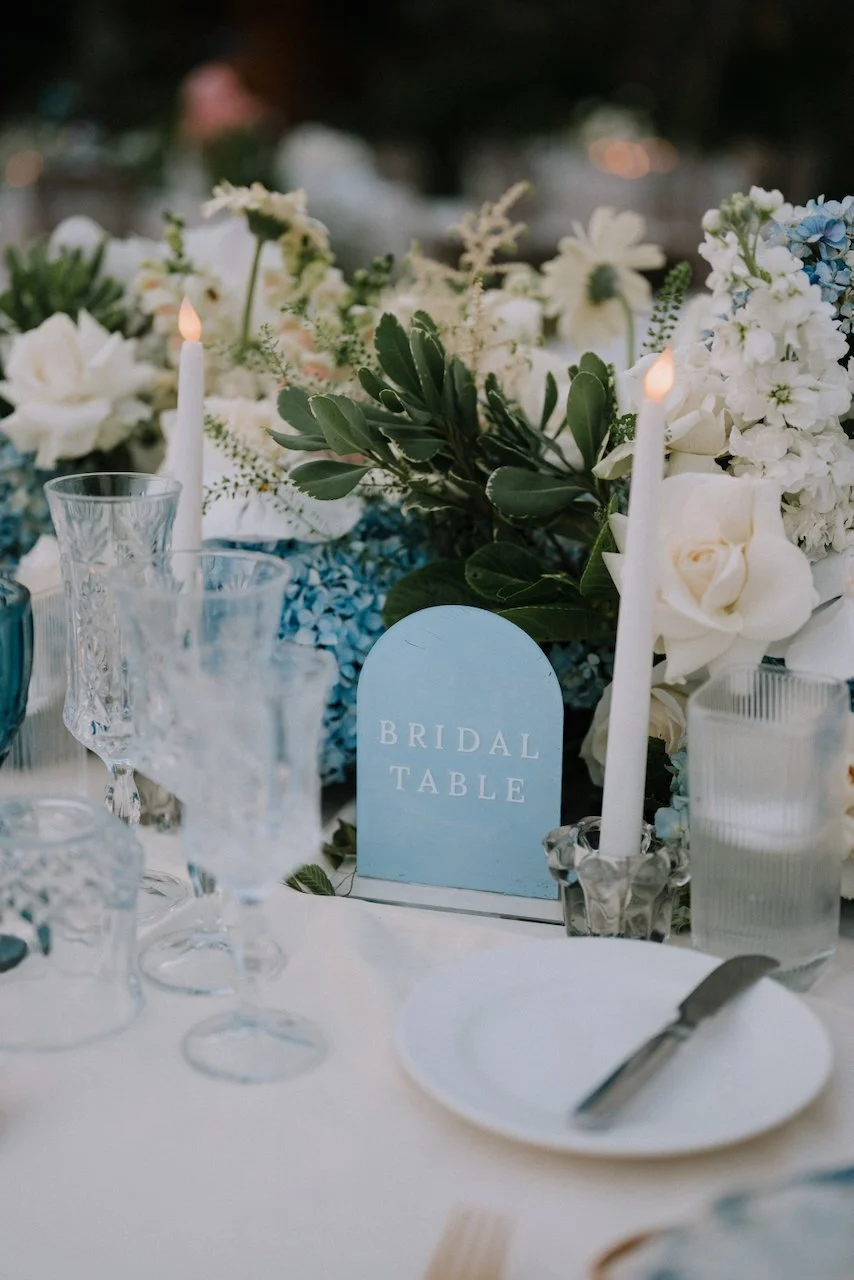Pale blue arched “Bridal Table” sign among blue hydrangeas, white roses and tapered candles