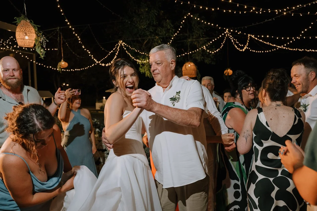 Kelly laughing as she dances with her father among guests at the Wonderland reception