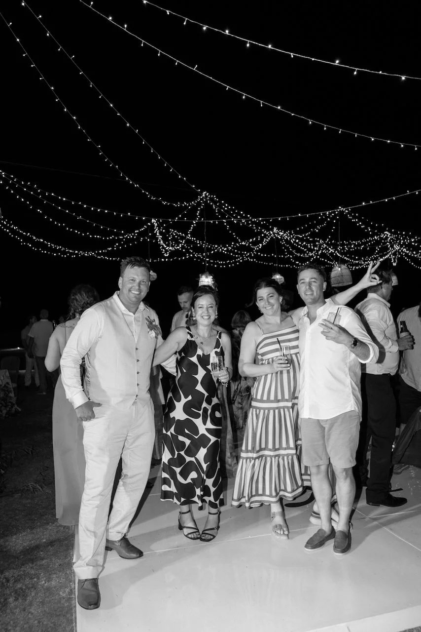 Black and white photo of Matt posing on the dance floor with three guests under the fairy lights
