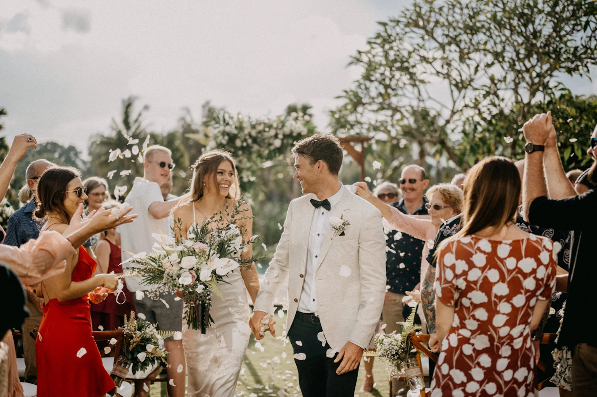 Bride and groom holding hands as guests throw petals at an outdoor Bali wedding, planned by Silver Lace Weddings.