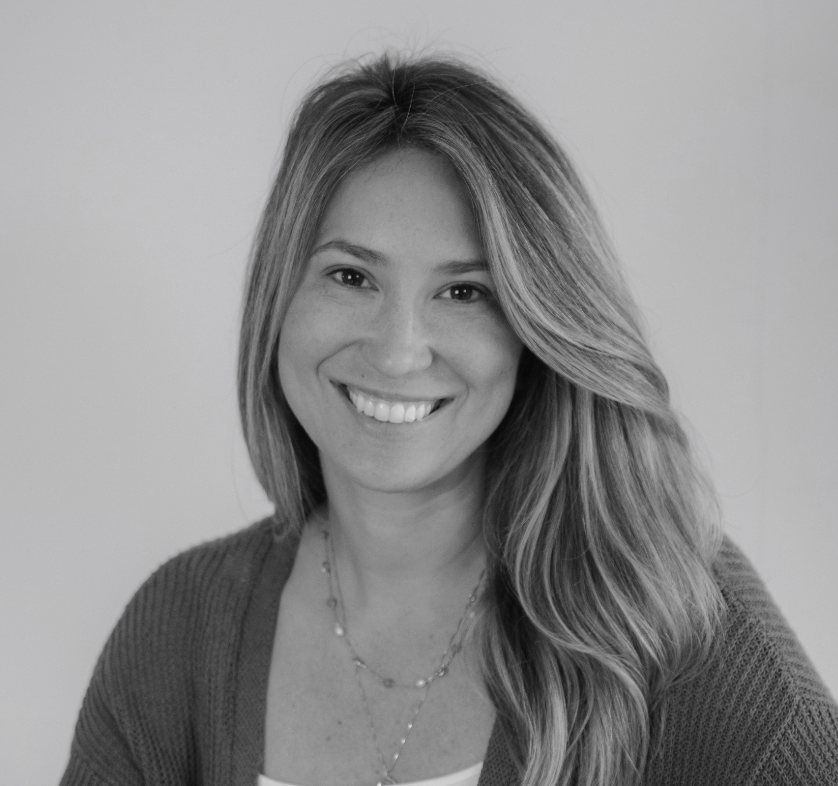 Black and white portrait of a smiling woman with long, wavy hair, wearing a necklace and a sweater.