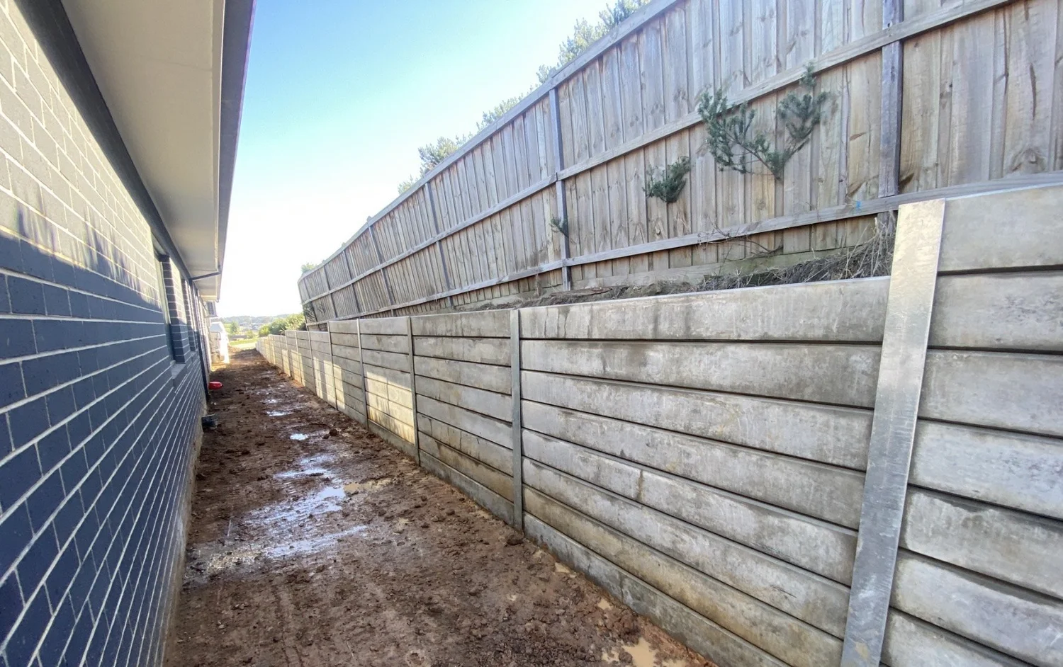 Timber sleeper retaining wall along a side boundary fence under construction