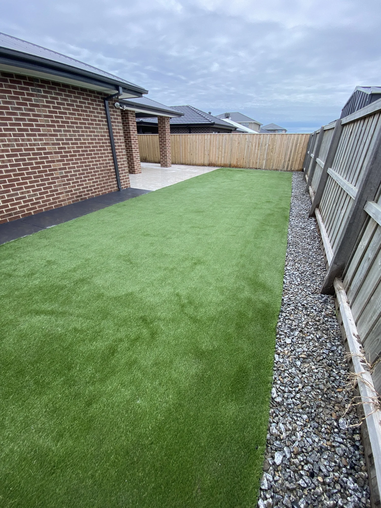 Synthetic turf strip with gravel edging along a side fence