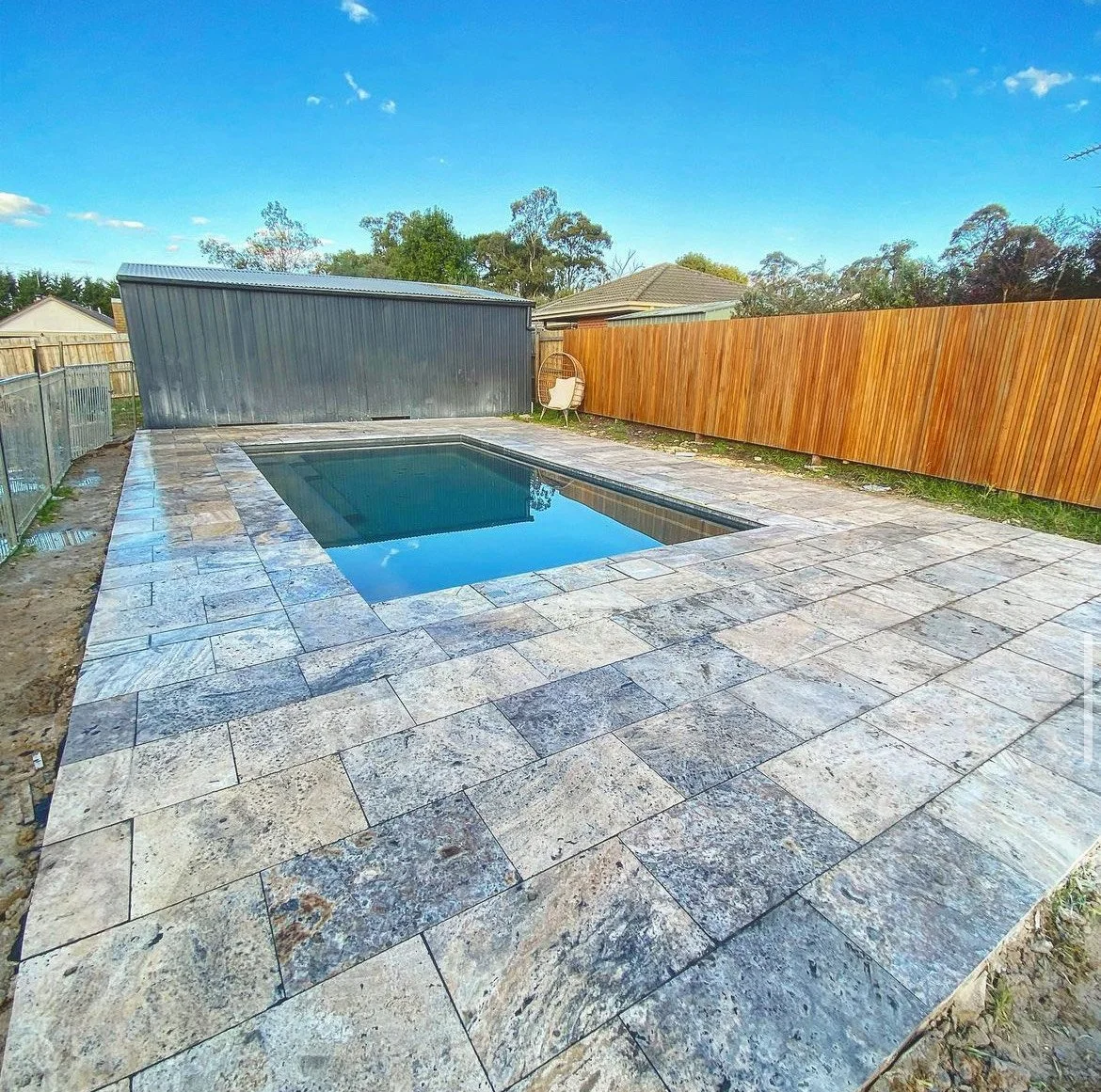Travertine-look paving around an in-ground swimming pool with timber fence