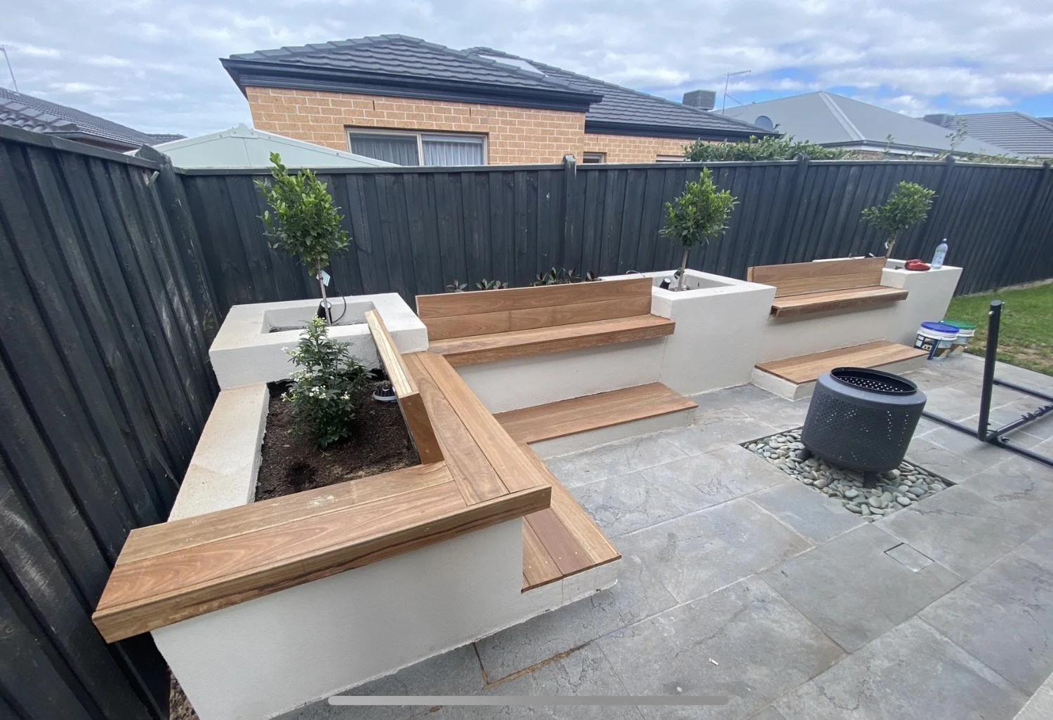 Backyard with rendered raised garden beds, timber bench seating and paved fire-pit area