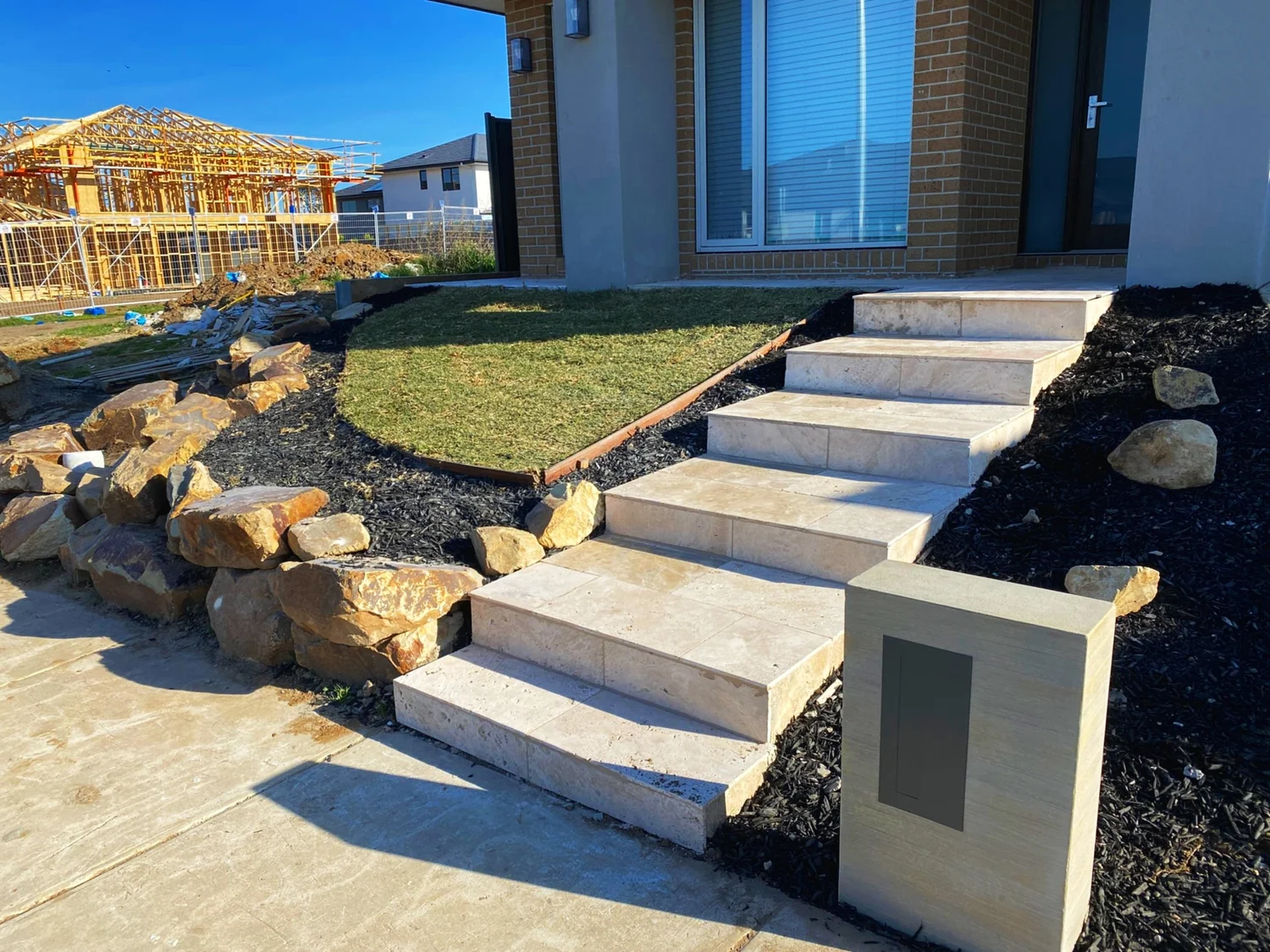 Sandstone-look block steps with rock boulders and lawn at a new home entrance