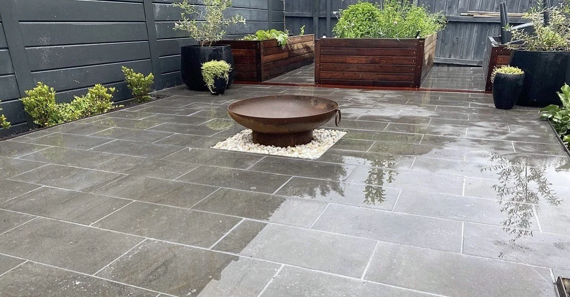 Large-format paved courtyard with round fire pit and raised planter boxes
