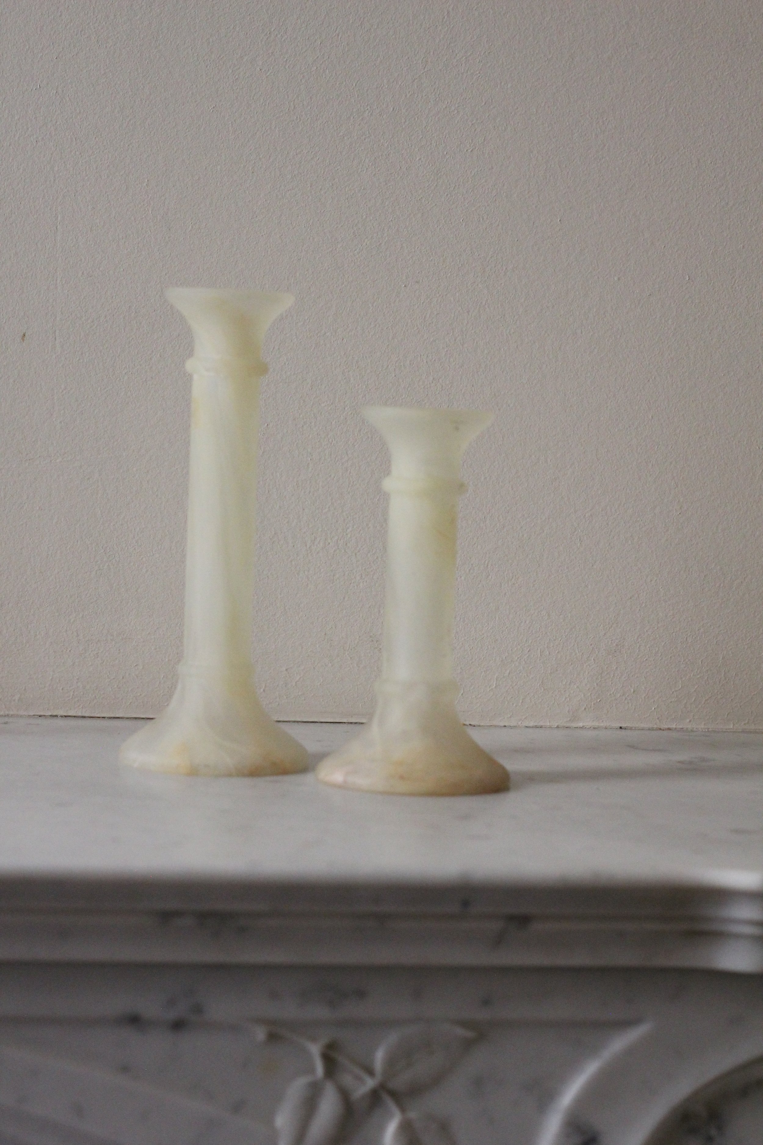 Two white marble candlesticks of different heights on a white marble surface against a gray wall. The candlesticks are made in Murano in Italy dating from 1950s.