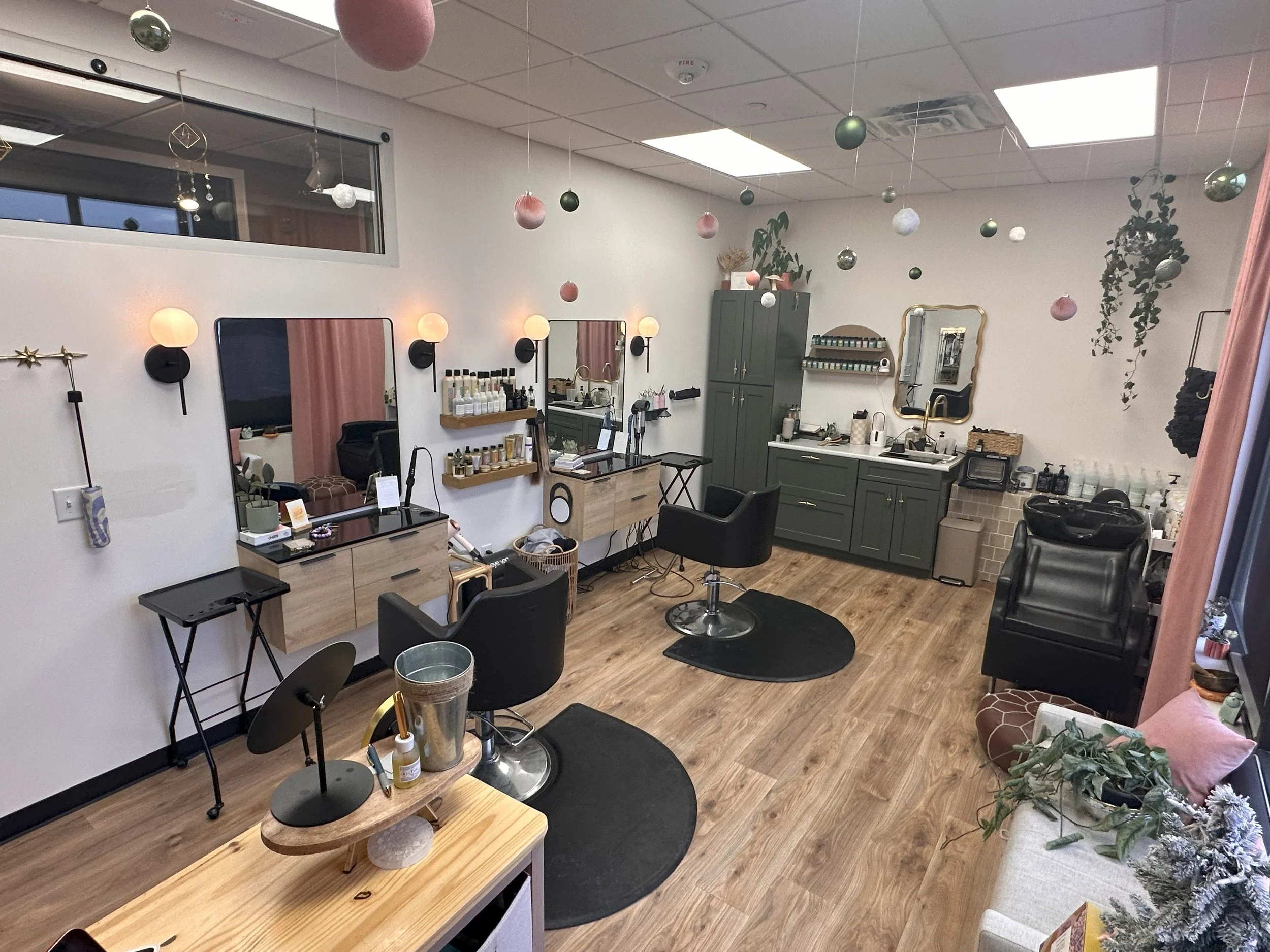 A modern hair salon with styling stations, mirrors, and chairs, decorated with hanging ornaments and plants.