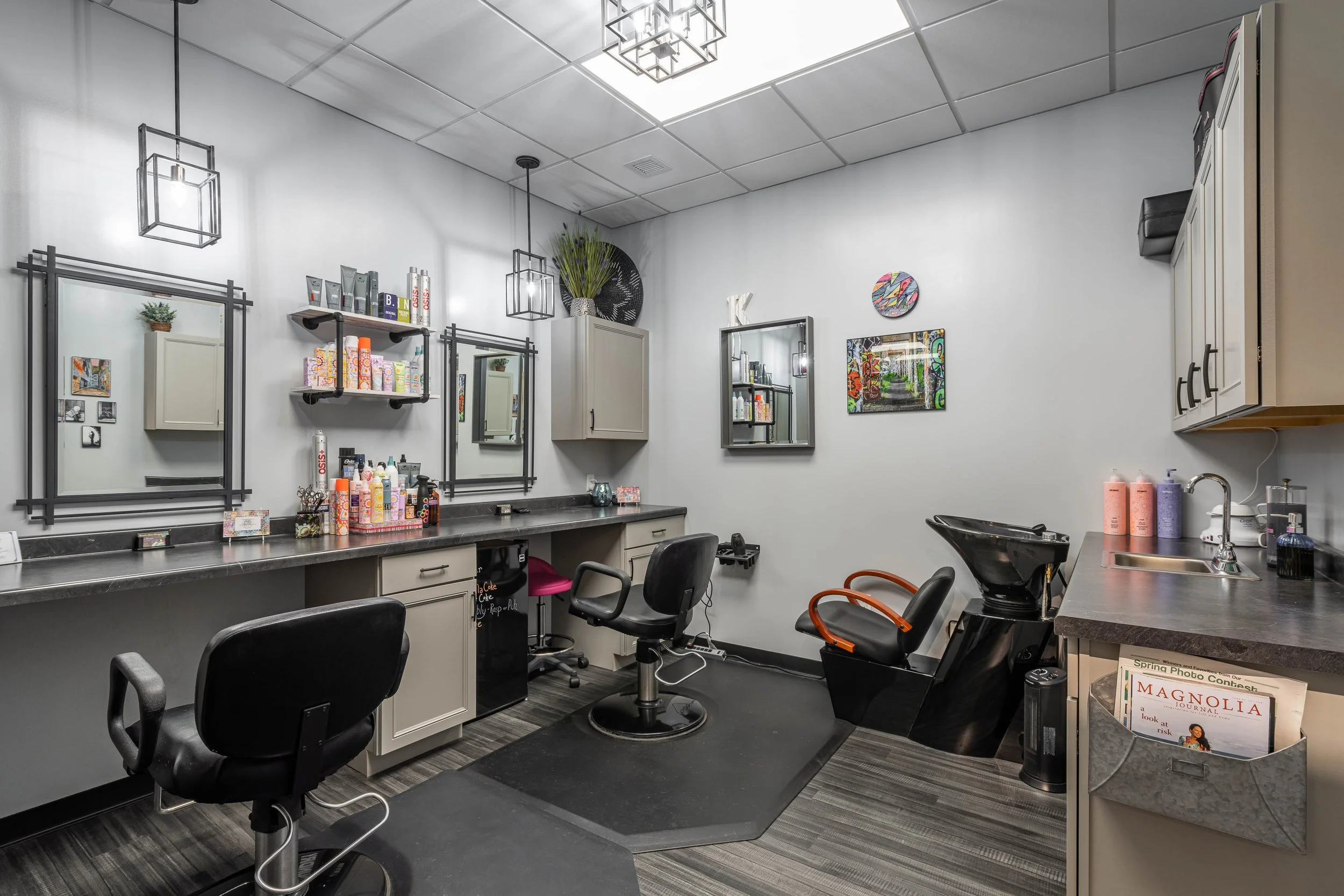 A hair salon with styling stations, mirrors, chairs, and hair washing sink, decorated with modern wall art and light fixtures.