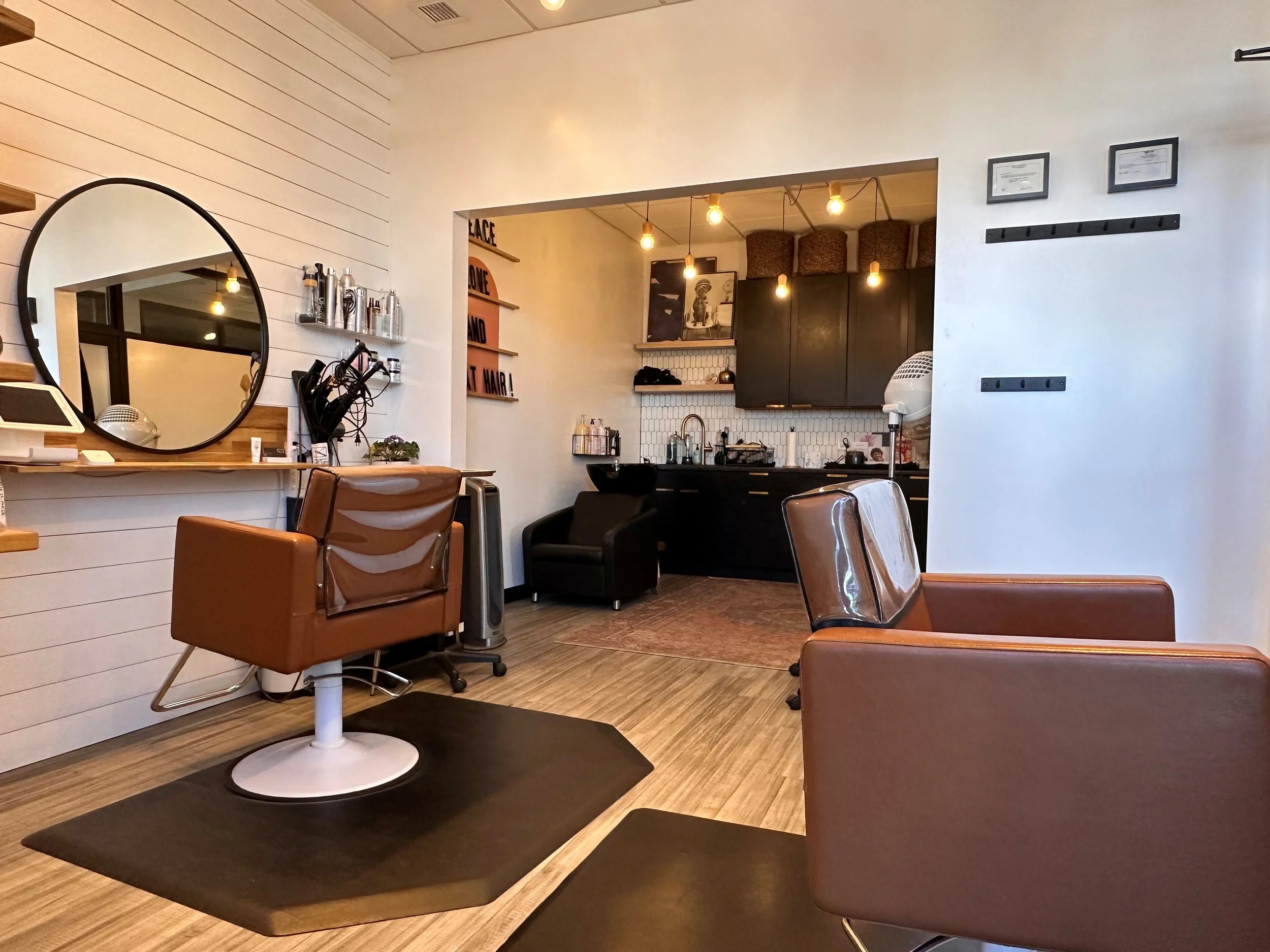 Interior of a modern hair salon with styling chairs, mirrors, and hair styling tools, featuring warm lighting and minimalist decor.