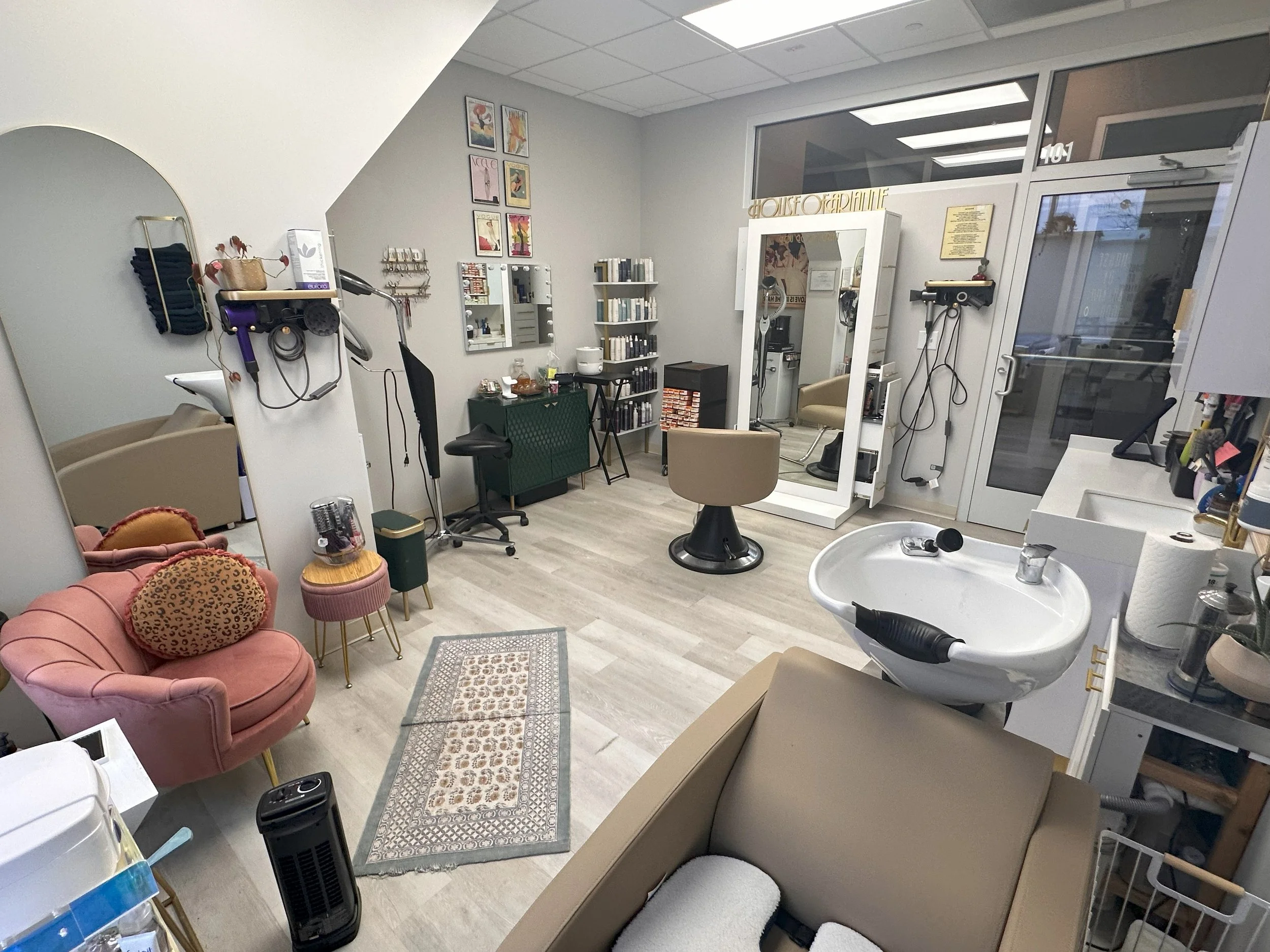 Interior of a beauty salon or hair studio with chairs, mirror, shelving, hair products, and a wash basin.