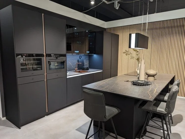 Een moderne keuken met zwarte kasten, een kookeiland met een marmeren werkblad, en een rustige decoratie met vazen en lampen.