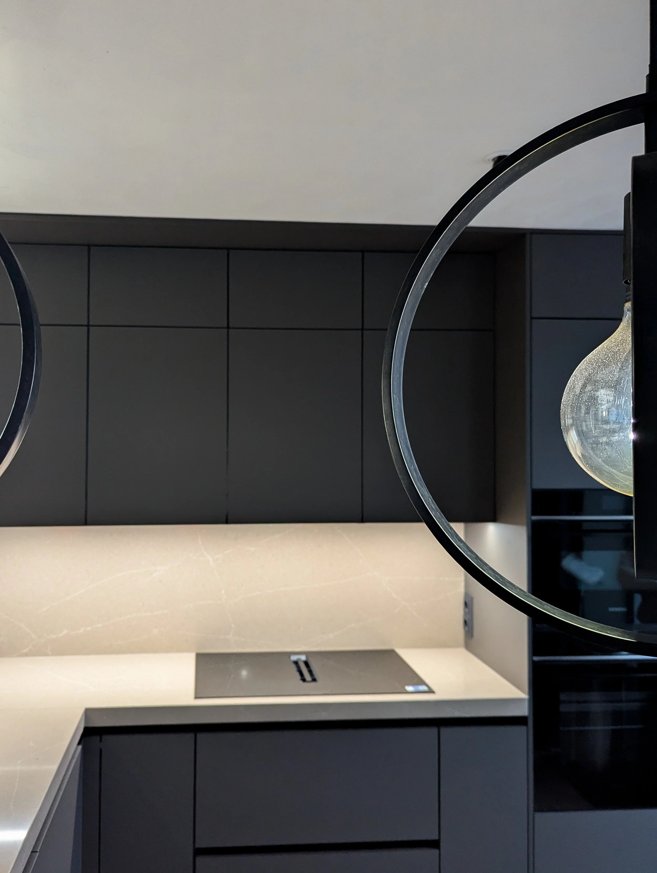 Moderne keuken met zwarte kasten en witte werkblad, plafondlamp met glazen bol, achterwand in donkere tegels.