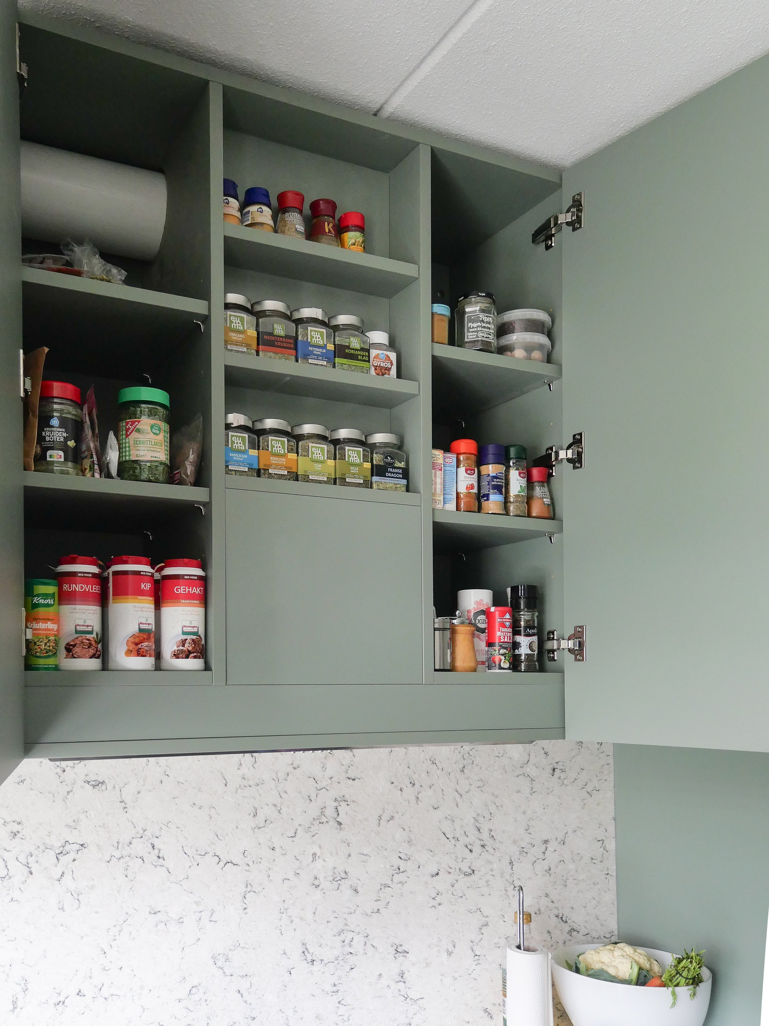 Open keukenkastje met potten, kruiden en specerijen, met een basket met groenten ernaast.