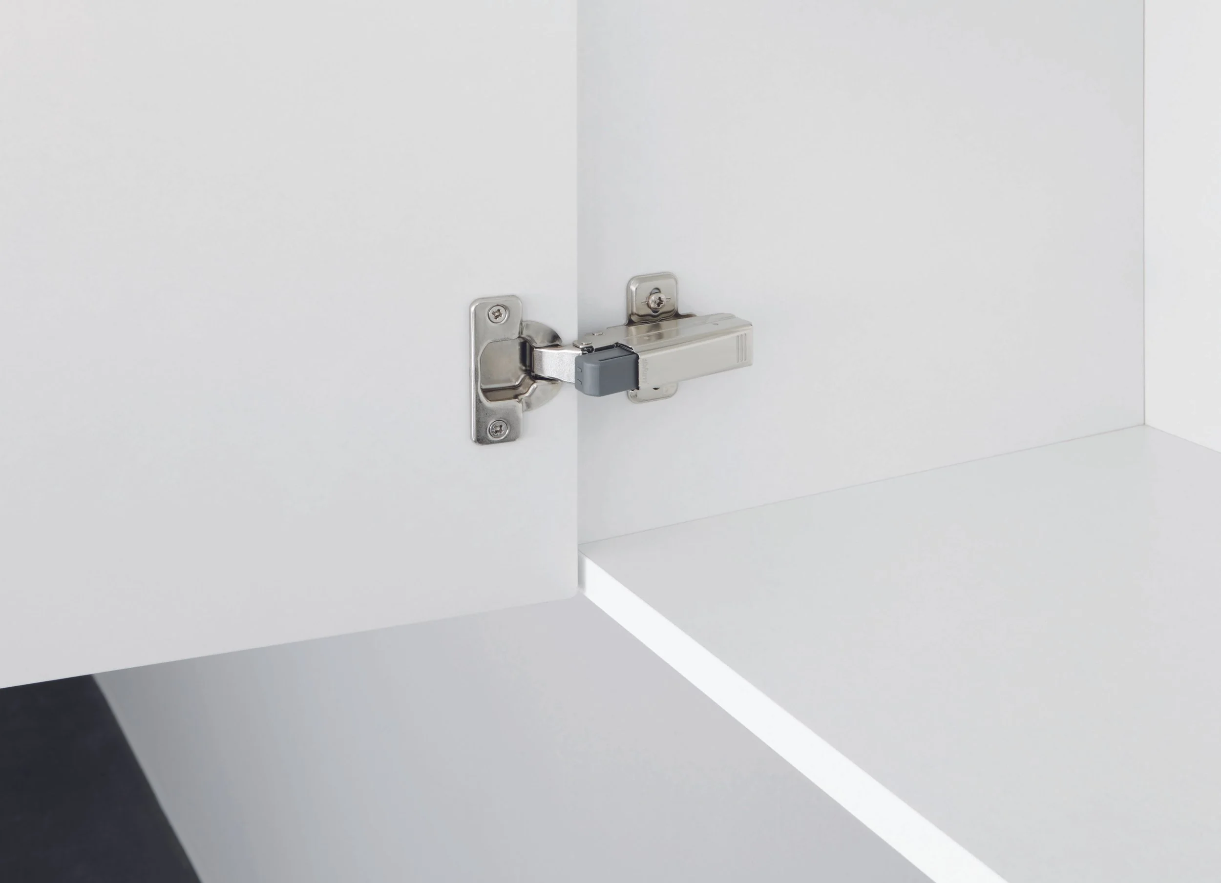 Close-up van een witte kastdeur met een verborgen scharnier en een veermechanisme aan de rand.