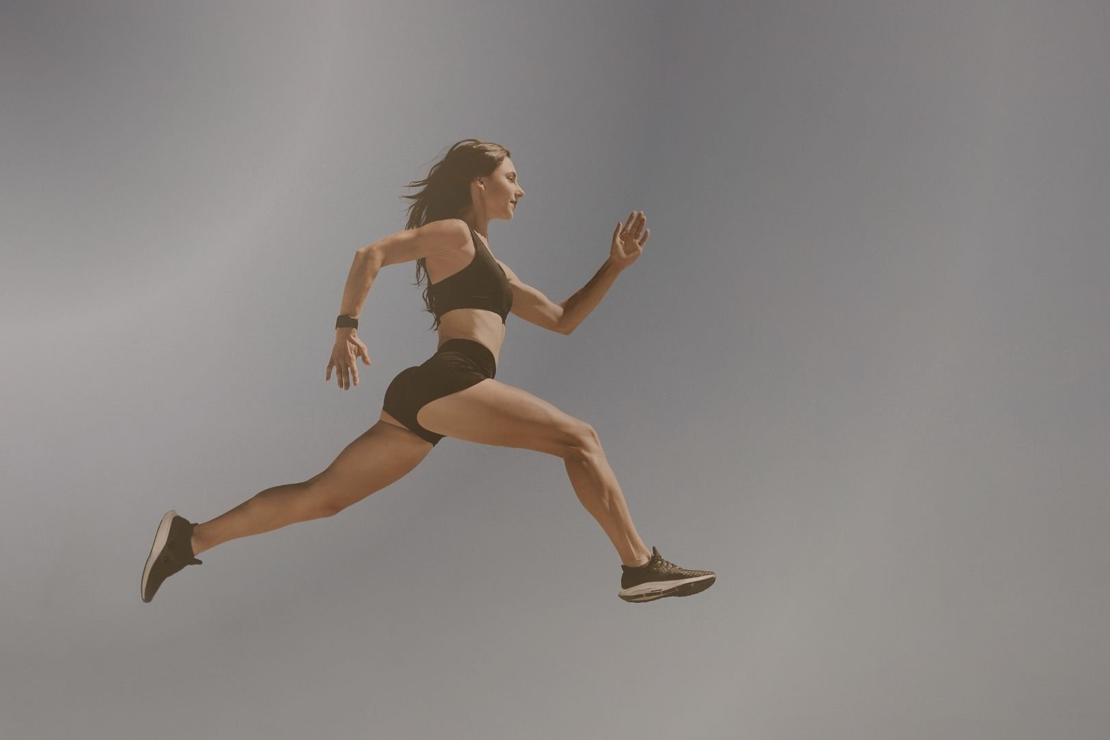 A woman in athletic clothing running fast in midair against a clear sky.