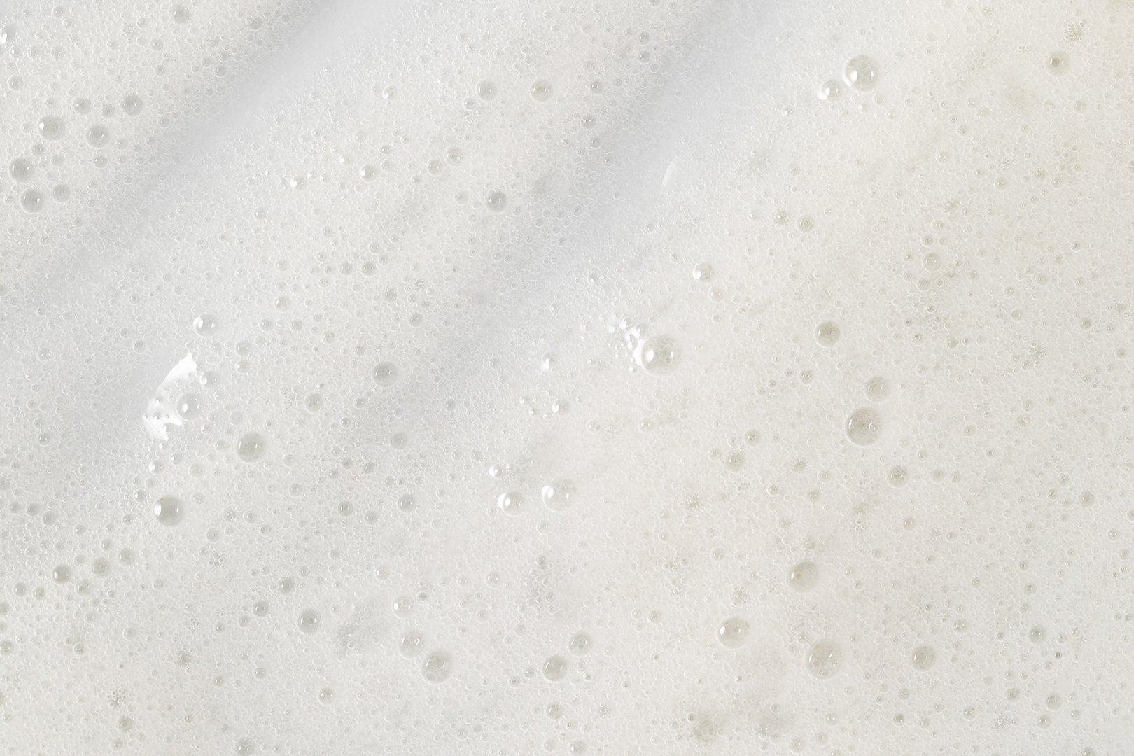 Macro texture of bubbly facial cleanser on white surface.