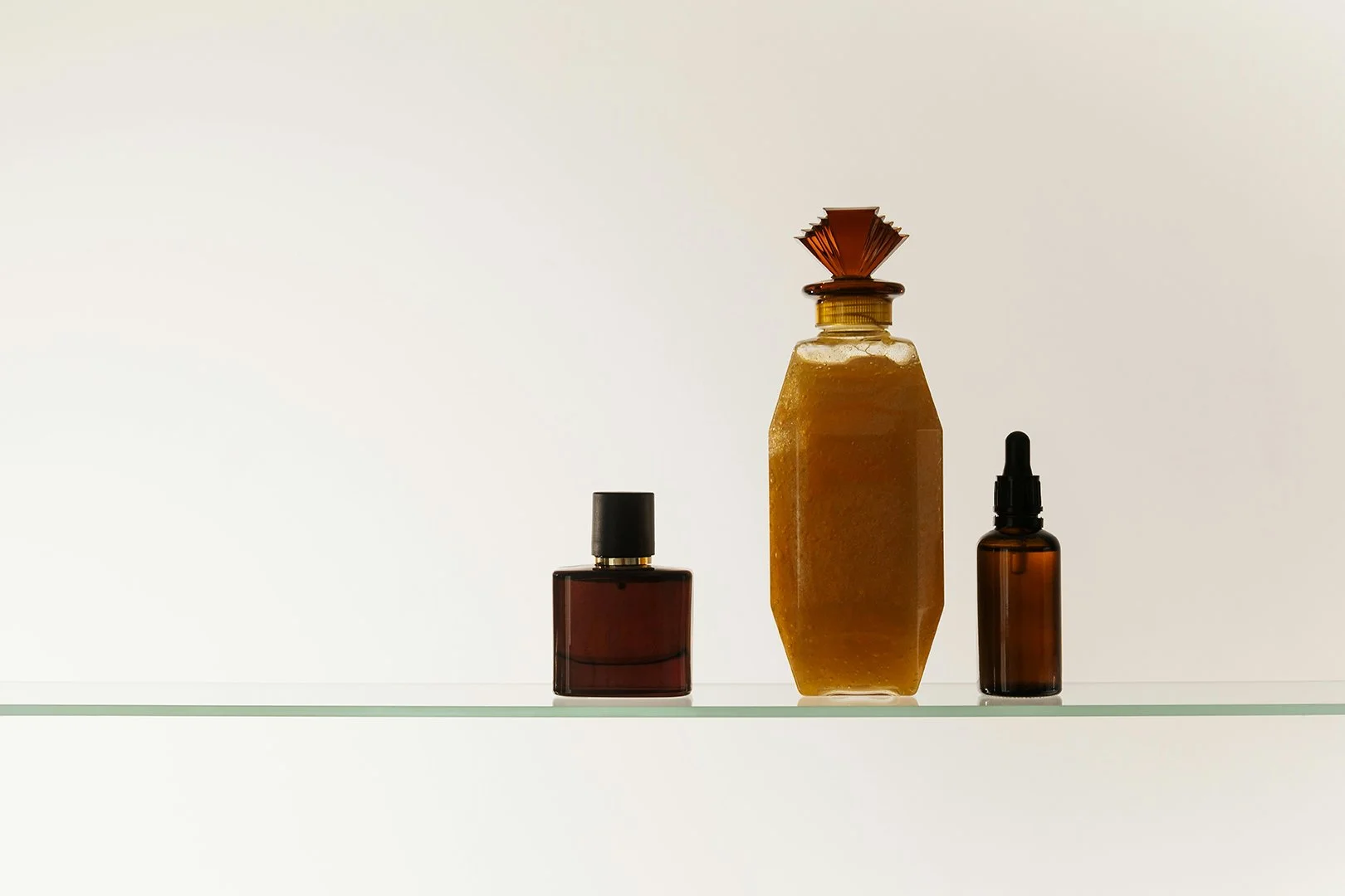 Bottles of fragrance and skincare on a glass shelf.