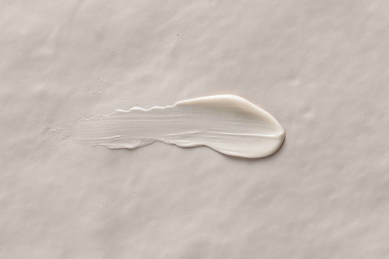Swatch of lip balm or moisturizer on textured beige background.