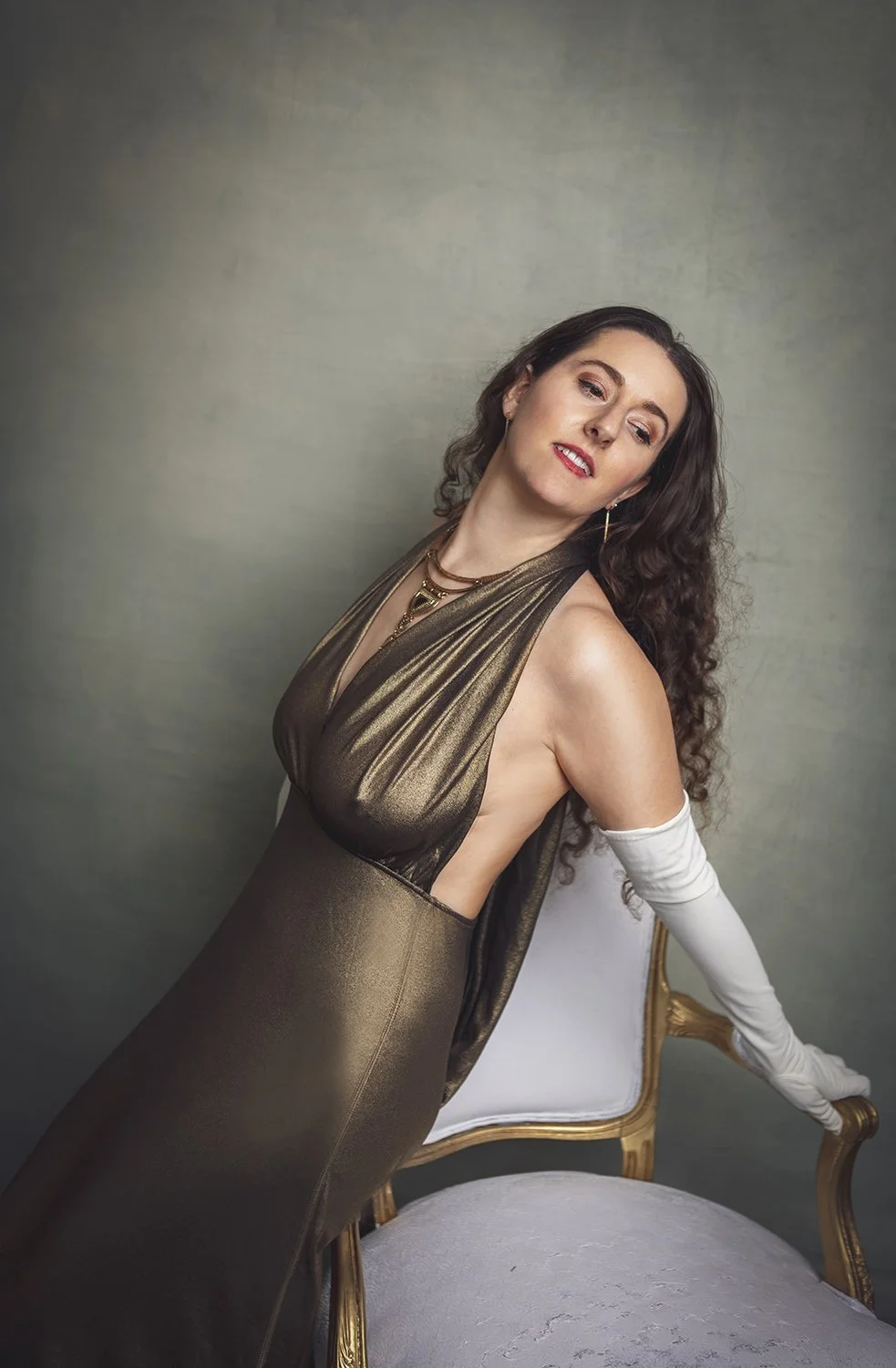 Woman leaning on a white chair during an elegant professional glamour portrait photoshoot.
