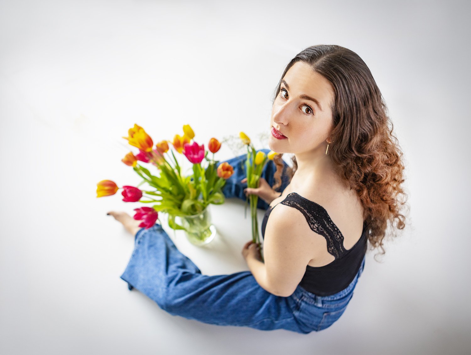 Woman with long hair wearing blue jeans and holding flowers during a professional portrait photoshoot