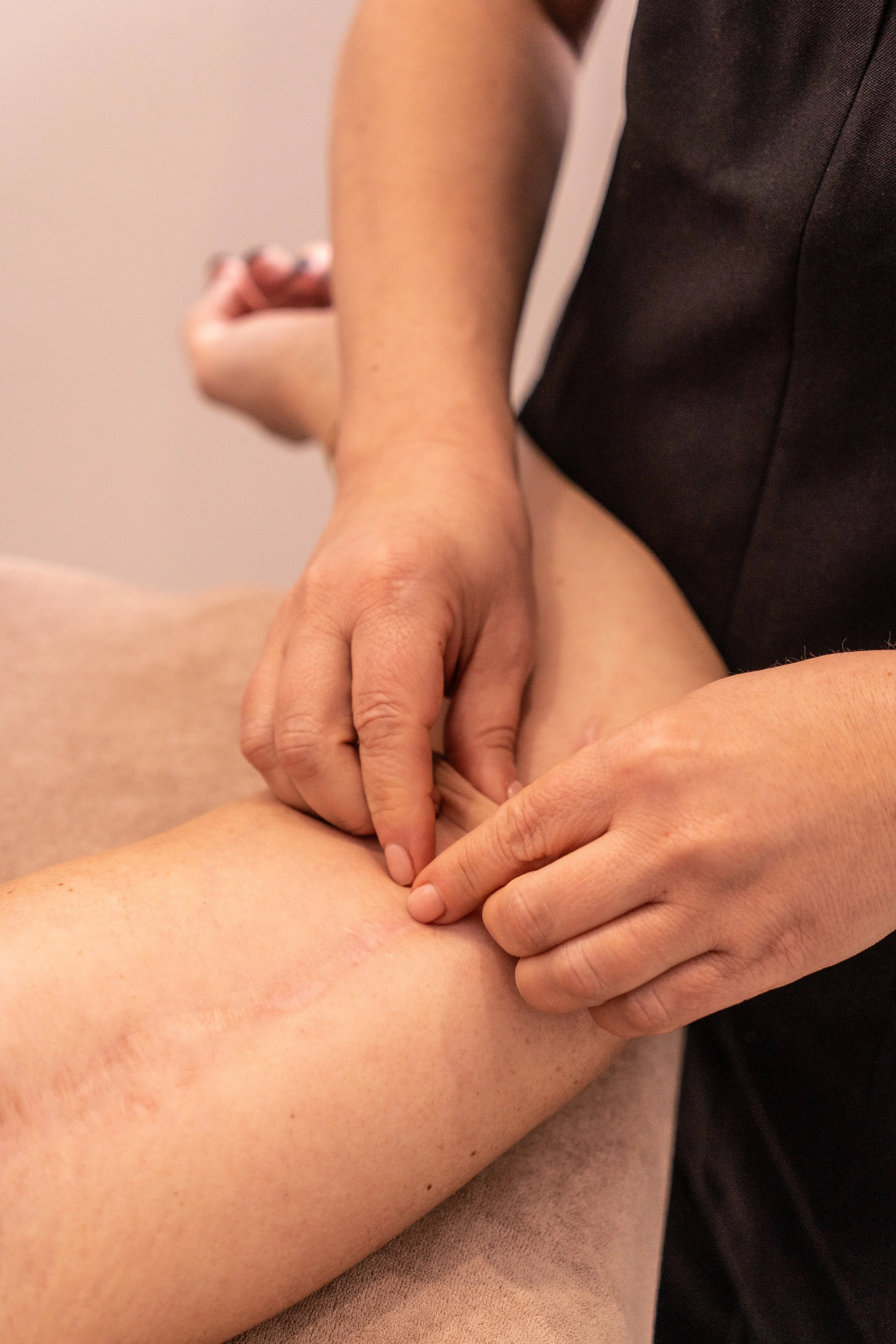 Une personne reçoit un massage ou une manipulation sur la cuisse, avec les mains d'un praticien, dans un environnement intérieur. Gros plan sur la peau et les mains.