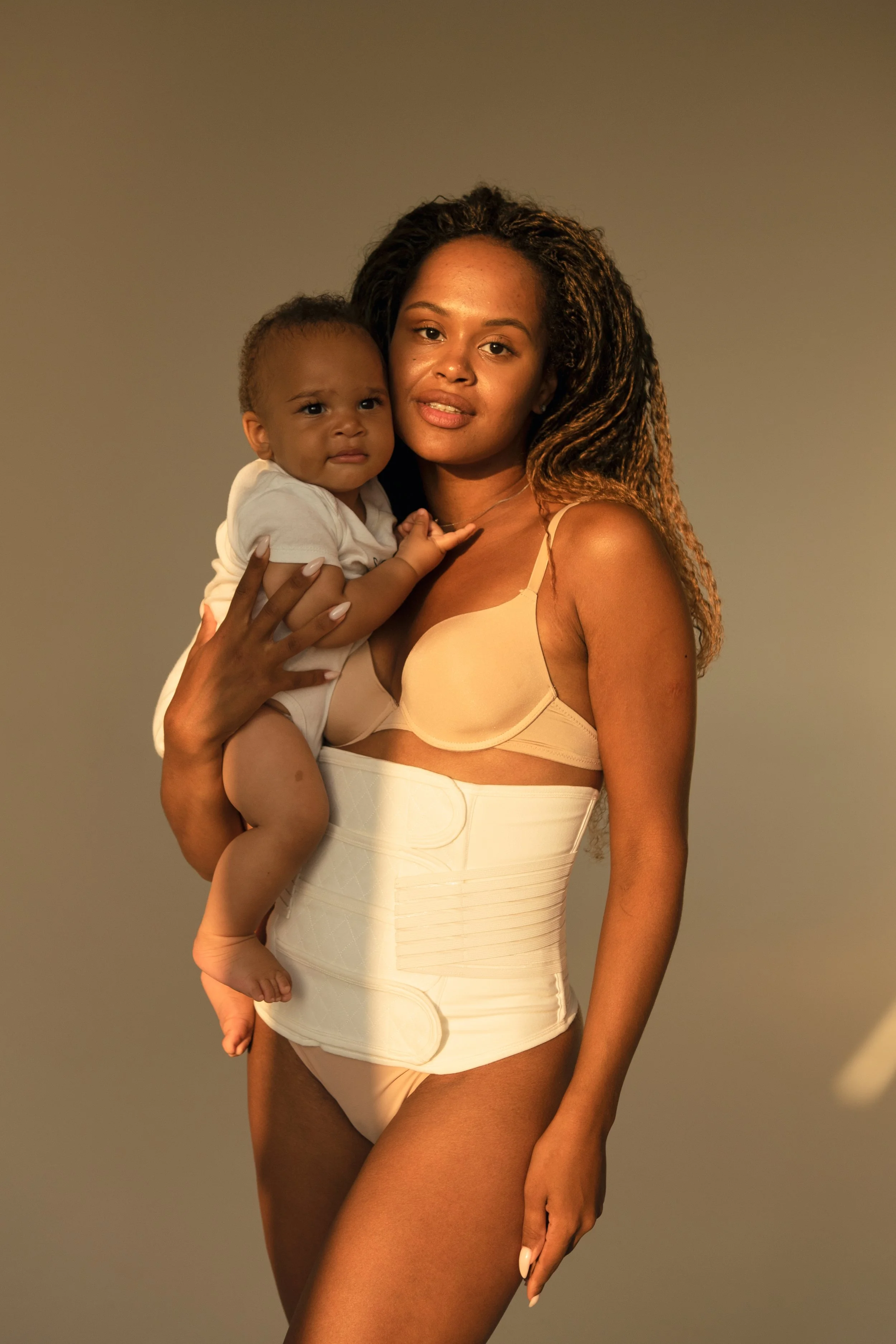 Une femme porte un enfant sur ses épaules dans un décor simple, avec un éclairage chaud.