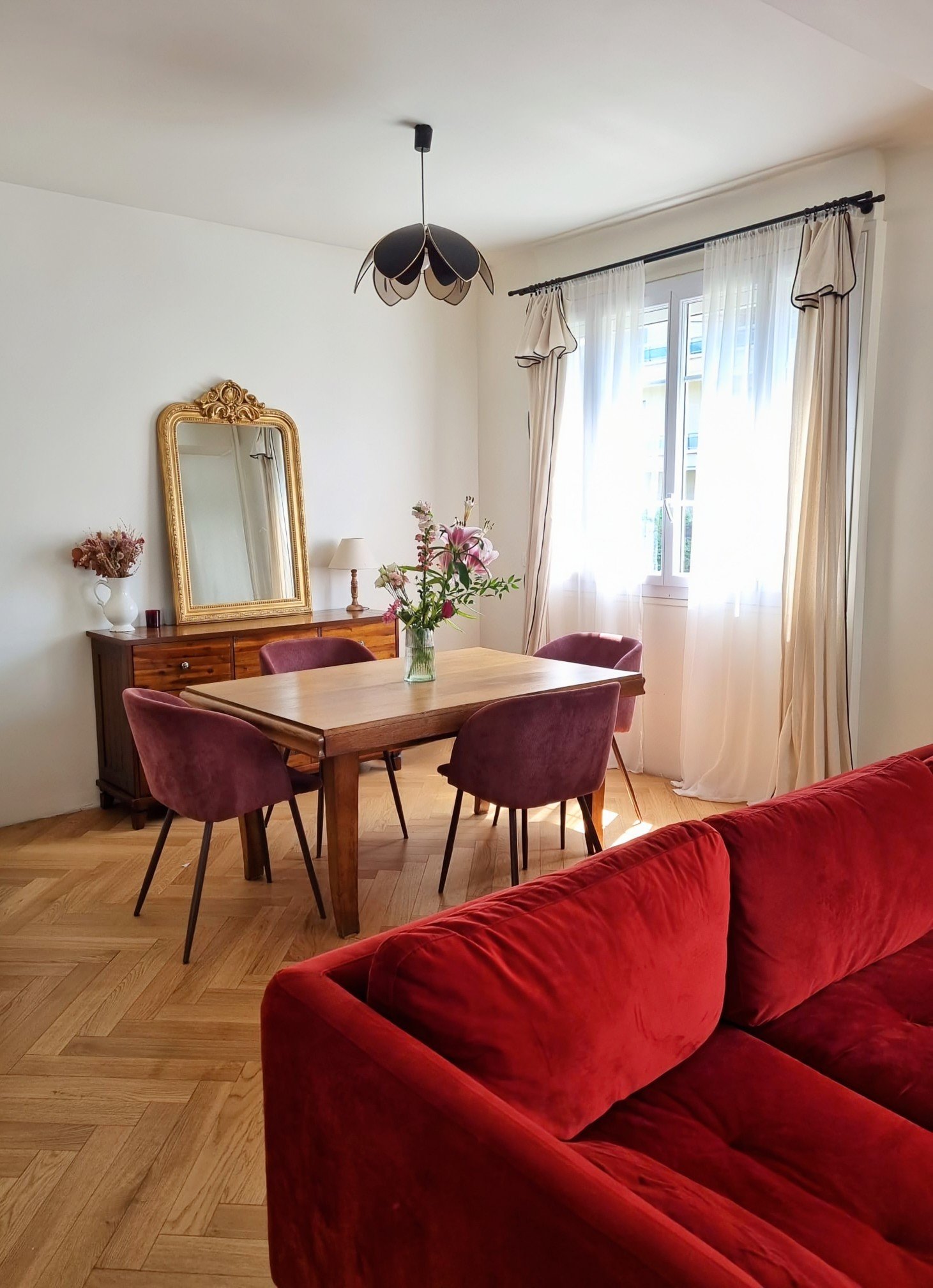 Elegant dining room in a Parisian townhouse featuring a modern dining table, a vintage sideboard with a 19th-century French gold mirror, and pink velvet chairs.