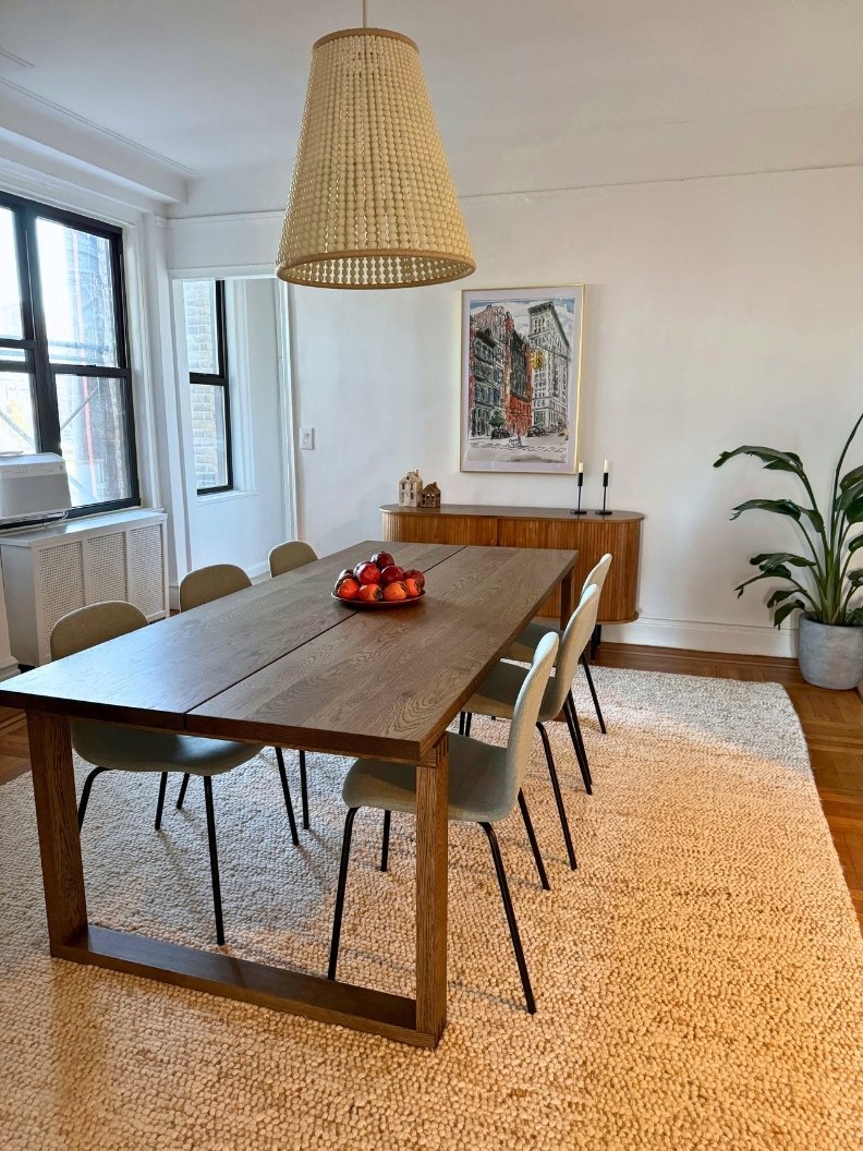 Dining room featuring a large dark wood table, a wood bead chandelier, a vintage sideboard, a large artwork, an indoor plant, a textured rug, and dusty blue dining chairs.